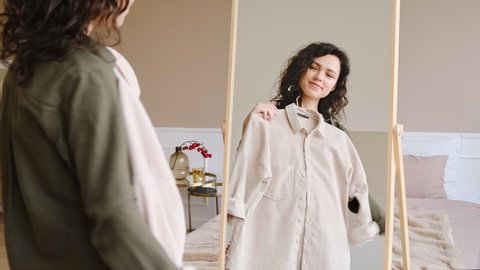 Young woman getting dressed looking in mirror. Trying on clothes enjoying herself. 