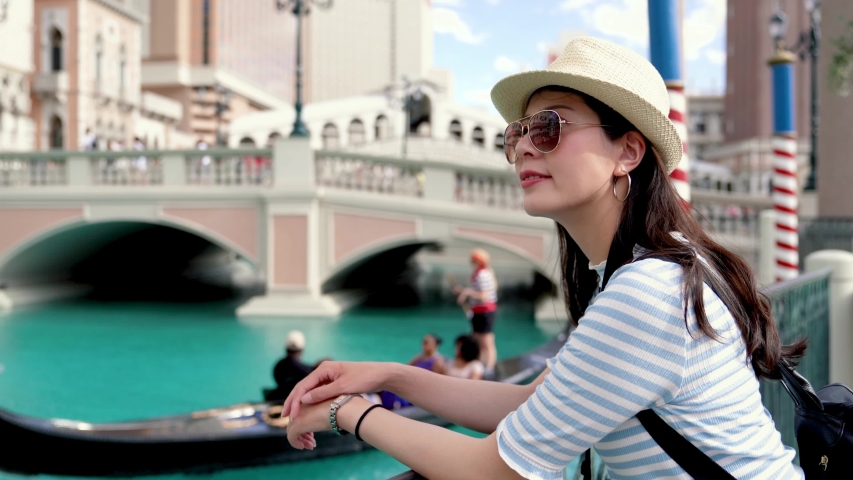 young girl traveler relax leaning on railing and standing by Gondola near Rialto Bridge in Venice Italy. blurred view of visitors sitting on boat and worker sailing on canal outdoors on sunny day.