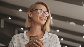 A beautiful smiling woman wearing eyeglasses is using a phone in a conference hall