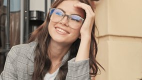 Positive dreaming young woman wearing glasses is smiling while looking to the side outside in the city center