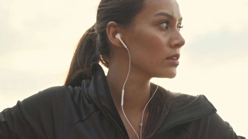 Close up view of Serious pretty asian sports woman in earphones warming up and looking away outdoors Royalty-Free Stock Footage #1044779029