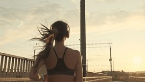 Back view of pretty asian sports woman in headphones listening music and running outdoors