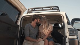 A positive beautiful couple man and woman are smiling and hugging while sitting in the car trunk