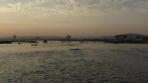 The drone flies over the river and over many boats with fishermen during dusk with the city and rural landscape in the background in Mali Aerial Drone Footage 4K