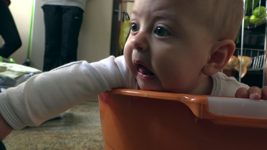Funny upset baby inside laundry bucket. Angry tearful toddler boy wanting attention