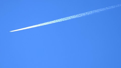 airplane and airplane trail high in clear blue sky.