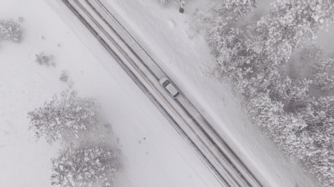 DRONE, TOP DOWN: Car drives through a slippery snow covered intersection in Spokane, Washington. Flying above a car driving down icy road as blizzard covers the landscape with a deep blanket of snow.