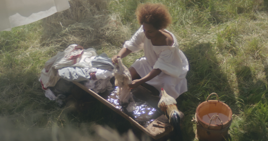 Top view of african woman washing clothes in old washtub in courtyard. Historical reconstruction. 19 century. North America, Southern States