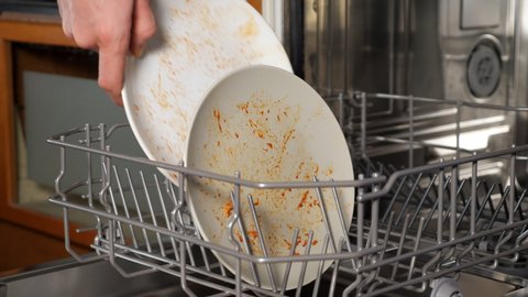 person puts dirty dishes and cutlery into modern dishwasher after having supper in kitchen extreme close view