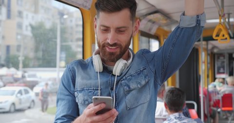 Young Handsome Bearded Man Using public Transport, Looking Happy and Pleasant. Chatting on his Mobile Phone. Search for popular songs and nice music at the App. Having Headphones