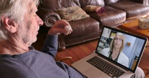 Elderly senior man holding a pill bottle saying goodbye to a female doctor during a telemedicine appointment on his laptop computer in his home