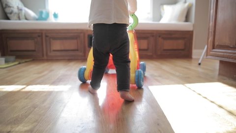 One year old child learning to walk, using a baby walker push toy in slow motion.