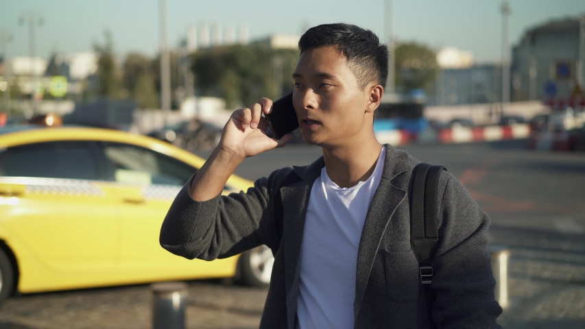 Real time portrait shot of a young Asian man speaking his location on the phone. Meeting in the center of Moscow.