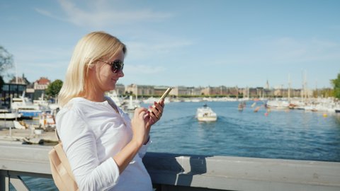 A woman uses a smartphone on a bridge overlooking Stockholm, Sweden