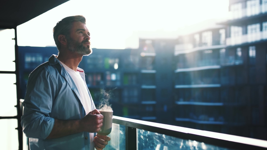Dreaming european middle aged man stands in the balcony with great views and drinks hot coffee or tea, sun shine, enjoying beautiful morning feeling happy slow motion | Shutterstock HD Video #1044823600