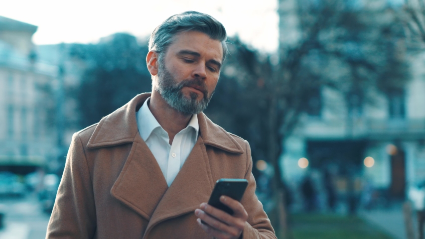 Close up view of smart caucasian businessman walks down the street uses phone texting scrolling tapping great morning technology communication sunny day successful | Shutterstock HD Video #1044823615