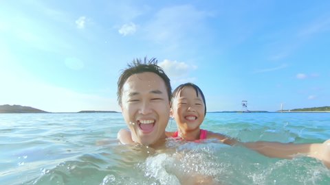 slow motion of asian little girl and her dad bathe in the sea and splash water