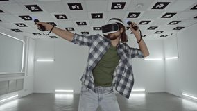 Young man in virtual reality glasses dances in a videogame in an empty playroom full of white neon illumination. Tracking arc shot, 360 degree