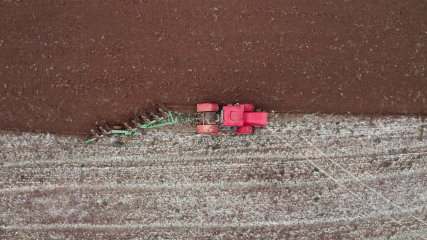 Aerial view of red tractor tilling snow covered field in winter