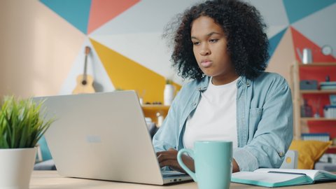 Slow motion of cute Afro-American woman using laptop at home writing in notebook taking notes busy with freelance work. People and technology concept.