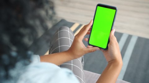 Back view of brunette holding chroma key green screen smartphone watching content without touching or swiping. Gadgets and contemporary people concept.