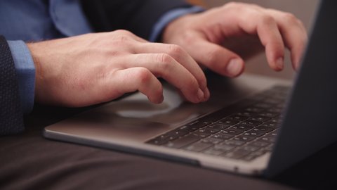 Closeup unrecognizible businessman finishing work on laptop at remote office. Man hands typing on notebook keyboard in slow motion. Successful business man browsing internet on laptop computer at home