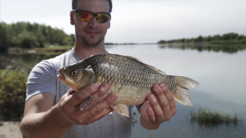 Angler holds the crucian carp (Cyprinus carassius) in hands and looks into the camera. Dolly zoom effect