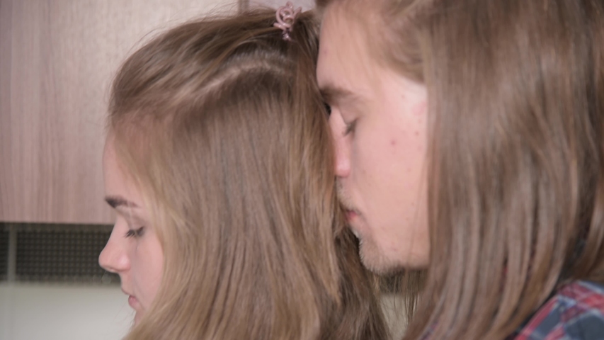 A long-haired young man hugs his girlfriend from behind, gently stroking her shoulder. Close-up