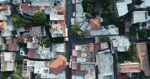 Aerial footage of traditional multicolored historic Greek houses with beautiful roofs of island city top down view. People walking on streets.