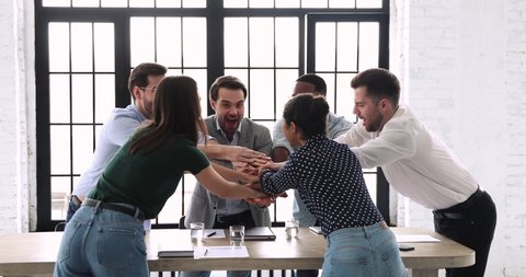 Happy reliable multi ethnic team staff business group stack hands together over meeting table express teamwork concept, strength in professional support, corporate partnership, power of collaboration