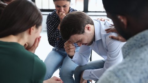 Sad desperate crying addicted alcoholic man share problem grief during group therapy session, diverse people helping supporting male patient having trauma depression at psychotherapy meeting concept