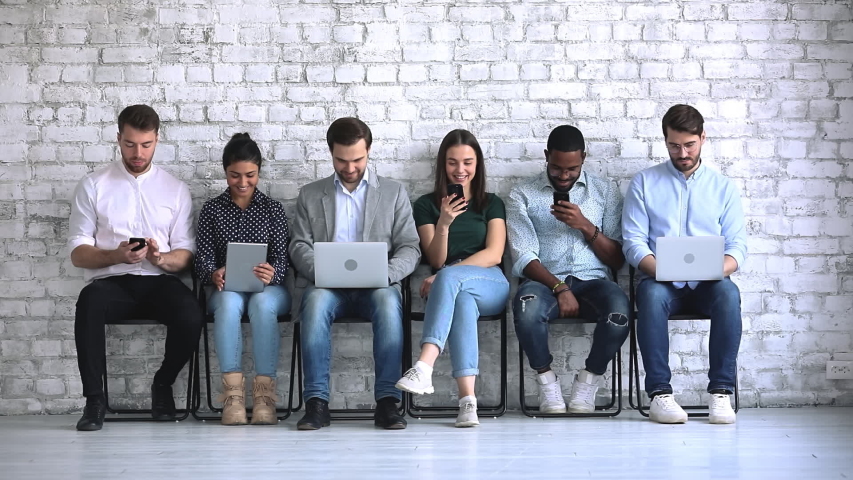 Six multiracial young business people sit on chairs in row waiting for job interview using tech electronic devices, diverse ethnic group obsessed with gadgets addicted digital life, recruit concept Royalty-Free Stock Footage #1044846403