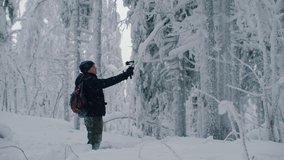 Man traveler blogger records video on action cam, looking at camera and talking in a background of snowy winter forest. Hiker shooting self video. Adventure, outdoors activities, healthy lifestyle.