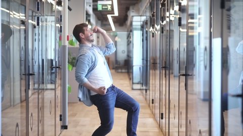 Excited young man employee manager entrepreneur celebrating business success, promotion, professional achievement or reward, dancing alone in modern office, making yes gesture while nobody watching.