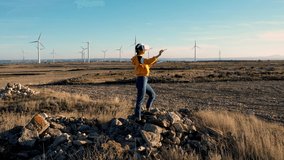 VIdeo of young hipster girl using vr glasses standing near windmill power station playing realistic simulation game gesturing during game
