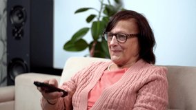 Senior Woman Using TV Remote Control. Zapping And Changing Channel. Grandmother With TV Remote Watching TV Channel Surfing Remote Control. Elderly Woman Relaxing Sitting On Sofa Watching Television - Powered by Shutterstock - Get 15% off with code: PIKWIZARD15