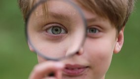 Closeup view of cute white young kid holding magnifier glass in hand and looking at camera through it smiling cheerfully. Real time full hd video footage. - Powered by Shutterstock - Get 15% off with code: PIKWIZARD15
