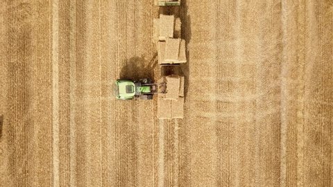 Drone shot of beautiful golden cornfield with a tractor stacking hay on cloudy but sunny summer day.