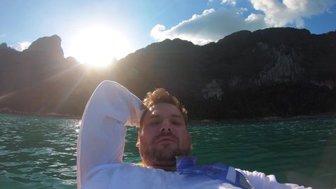 The blogger guy is lying on a kayak on the lake and takes selfie for social networks on Instagram,a beautiful natural landscape behind him,mountains,the sun,wildlife and the jungle.A man travels