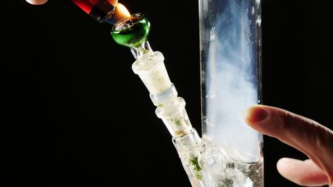 Burn marijuana in a glass Bong.The smoke is passed through water for cooling.Close-up,black background,smoke.The hand grips the hole in the Bong for smoke.Hookah Smoking.The legalization of cannabis.