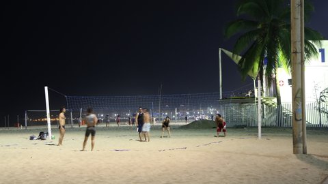 Rio de Janeiro, Brazil - January 17, 2020: Night timelapse of people playing beach volleyball in Copacabana near Leme. City light visible in the background. 