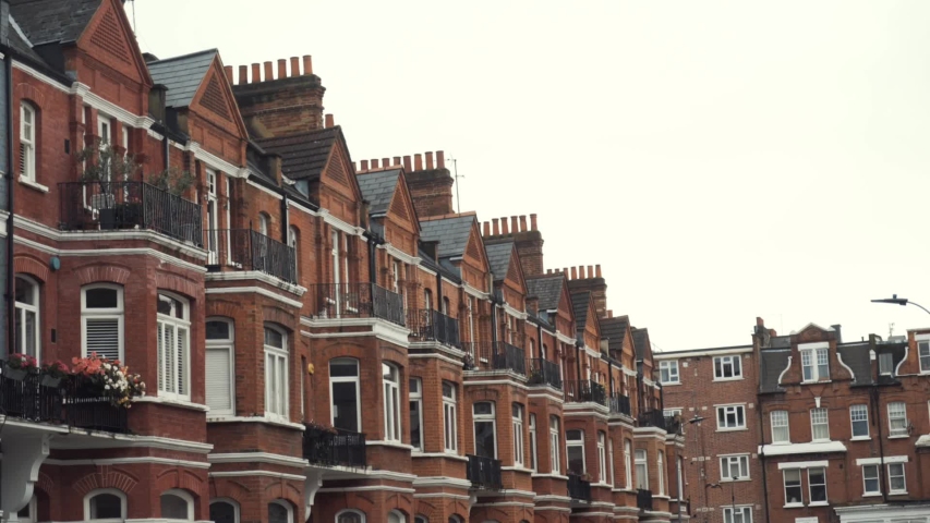 Close-up of Row of typical English terraced brick houses against the grey sky in autumn day. Action. Traditional English architecture Royalty-Free Stock Footage #1044910399