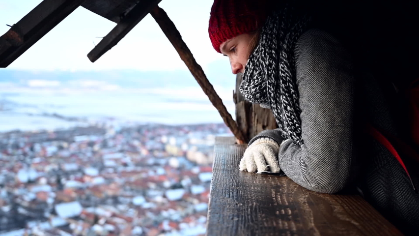 Woman watching a village and snowy landscape from the heights with winter clothes