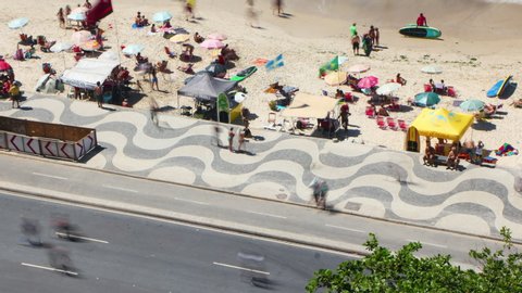 Rio de Janeiro, Brazil - January 17, 2020: Aerial timelapse of Copacabana street and walkway with traffic and people walking on the beach. View of the ocean, chairs, shops and swimmers 