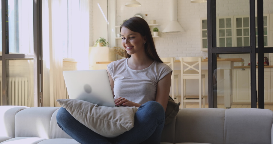 Happy young woman relaxing on sofa with computer, chatting with friends online in social network, answering messages emails, web surfing information, shopping in internet store in cozy studio home. Royalty-Free Stock Footage #1044920689