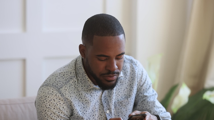 Happy african american young man reading sms on mobile phone, recording voice answer in social network. Smiling biracial guy chatting online with friends, dictating audio messages, using smartphone. Royalty-Free Stock Footage #1044920773