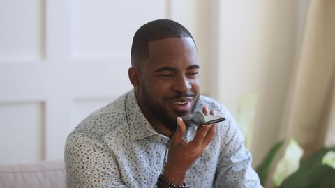 Happy african american young man reading sms on mobile phone, recording voice answer in social network. Smiling biracial guy chatting online with friends, dictating audio messages, using smartphone.