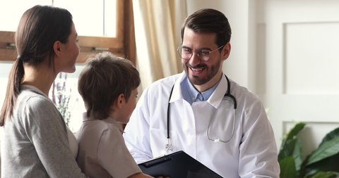 Happy caring kind male surgeon pediatrician support encourage kid boy patient at pediatric checkup meeting, smiling professional paediatrician talk to healthy child and mom visit doctor in hospital