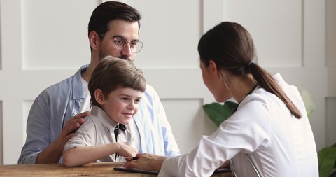 Caring kind professional female pediatrician consulting stroking child boy giving high five to happy healthy cute preschool patient visiting doctor with father, paediatric medical healthcare concept