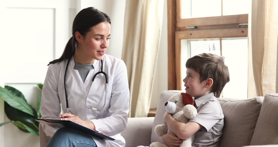 Caring professional female doctor nurse pediatrician talk to cute preschool child boy patient hold toy sit on sofa at medical consultation, children healthcare treatment pediatric checkup concept